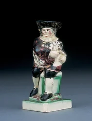 Dick Whittington kannu, muotoiltu nousemassa korkeaselkätuolista, pitelee kissaansa, roiskunut ruskeissa, vihreissä ja mustissa vaatteissa, muotoiltu kilpi kyljellään, n. 1790