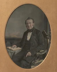 Istuva mies osoittaa kohtaa avoimessa kirjassa, 1850-luku.