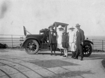 Ryhmä ihmisiä autonsa edessä meren rannalla, 1920-luku