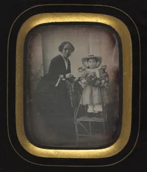 Lapsi seisoo tuolilla ja pitelee kukkia, äidin kanssa, c. 1855.