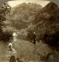 Heinää vuoristohyllyllä korkealla Marokin kylän ja peilikirkkaan Geirangerfjordin yläpuolella, Norja, c1905