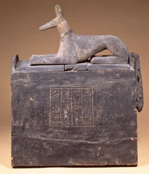 Plyonin muotoinen shabti-laatikko, jonka kannessa on teksti ja Anubis-patsas sakaalina (myöhemmin syntyneenä), egyptiläinen, Thebasta, 22. dynastian alkupuolelta, noin 900 eKr. (mustaksi maalattu puu)