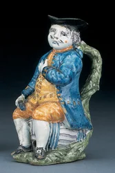 Toby-kannu vaalean mangaanin kasvot ja kädet, pitelee ja tyhjä pallomainen ruskeanvärinen kannu pesty sininen takki ja ratsastushousut ja vihreä liivi, n.1800