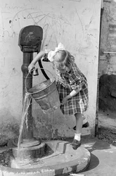 Pikkutyttö tyhjentää vesiämpäriä pumppulähteessä, 9. toukokuuta 1939 (s/w-kuva).