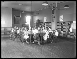 Lapset kuuntelevat naista Queens Borough Public Libraryn tunnistamattoman haarakonttorin lukusalissa, noin 1910.