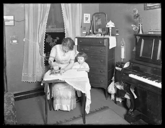 Tuntematon nainen esittelee sähkösilitysraudan käyttöä pikkutytön katsomassa, n. 1913-14