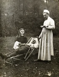 Lääkäri mittaa loukkaantuneen miehen pulssia sairaanhoitajan apuna, noin 1900 (m/v kuva)