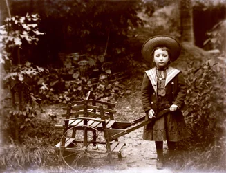Tyttö kärryineen puutarhassa, 1900-luvun alku (b/w kuva)
